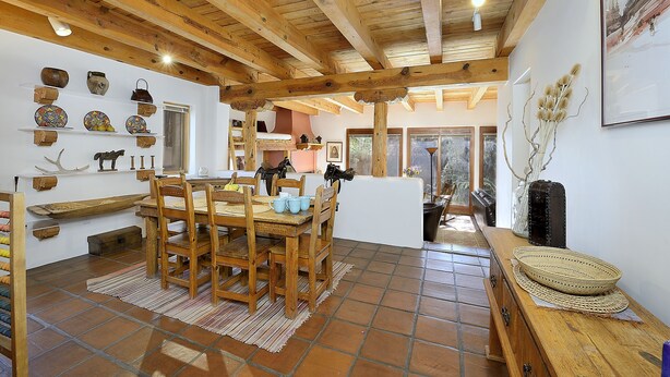 Un interior rústico con vigas de madera a la vista, una mesa de comedor de madera y suelo de baldosas.