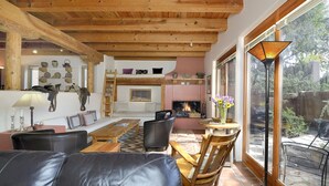 Una sala de estar acogedora con chimenea, vigas de madera y un gran ventanal con vistas a un jardín.