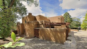 Un edificio con fachada rústica de adobe, rodeado de grava y vegetación.