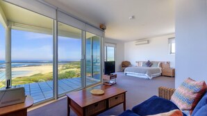 Un dormitorio con un gran ventanal corredera que da a un balcón con vistas al océano y la playa.
