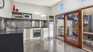 Eine moderne Küche mit Edelstahlgeräten, inklusive Backofen und Kühlschrank. Durch eine Schiebeglastür ist ein Essbereich mit Tisch und Stühlen zu sehen.