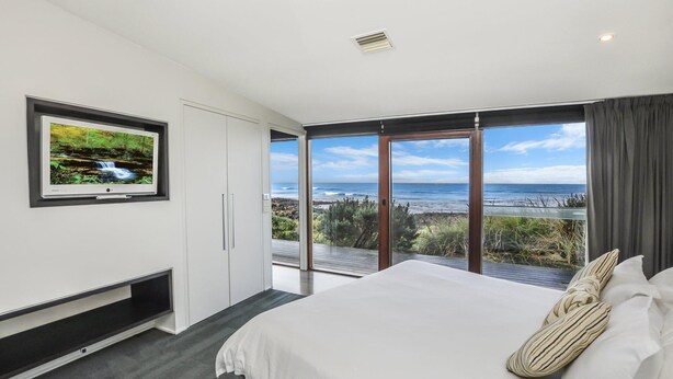 Ein Schlafzimmer mit Bett, Fernseher und einem Balkon mit Meerblick.