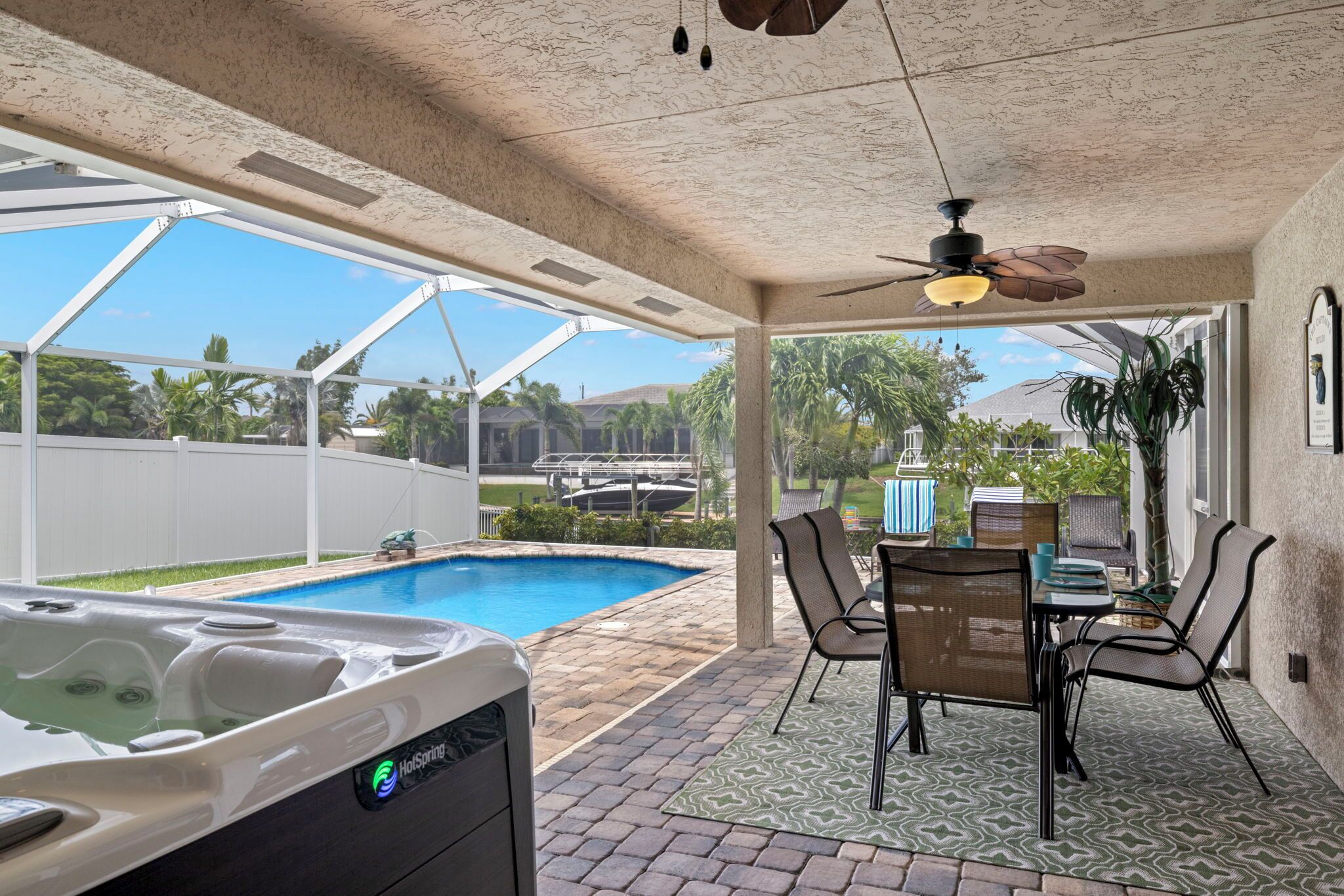 A covered patio with a hot tub, outdoor seating, and a view of a swimming pool.