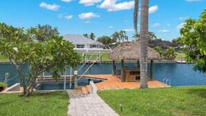A dock extending over water with a thatched-roof structure, a wooden deck, and a clear sky. - Fully stocked & Pet Friendly! Bikes, pool table, hot tub & more! Villa Aleena - SWFL Rentals (Cape Coral)