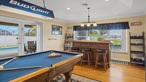A pool table in a room with a bar area, a pool, and a view of the outdoors. - Fully stocked & Pet Friendly! Bikes, pool table, hot tub & more! Villa Aleena - SWFL Rentals (Cape Coral)