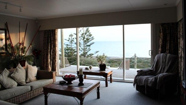 A living room with a sofa, a coffee table, and a view of the ocean through large windows. - Relax in the Wanganui Dunes (Wanganui Township)
