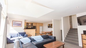 Un appartamento moderno con zona soggiorno, cucina e sala da pranzo. Si vedono un divano, un tavolino da caffè e un televisore montato a parete.