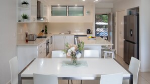 Une cuisine moderne avec des meubles blancs, un îlot central et un coin repas comprenant une table et des chaises blanches.