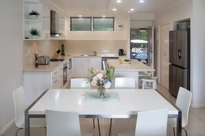 A modern kitchen with white cabinetry, a central island, and a dining area with a white table and chairs.