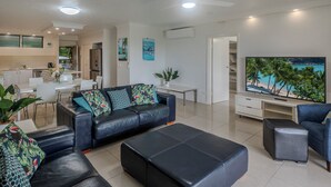 Un salon moderne avec un canapé, un pouf et un téléviseur à écran plat.