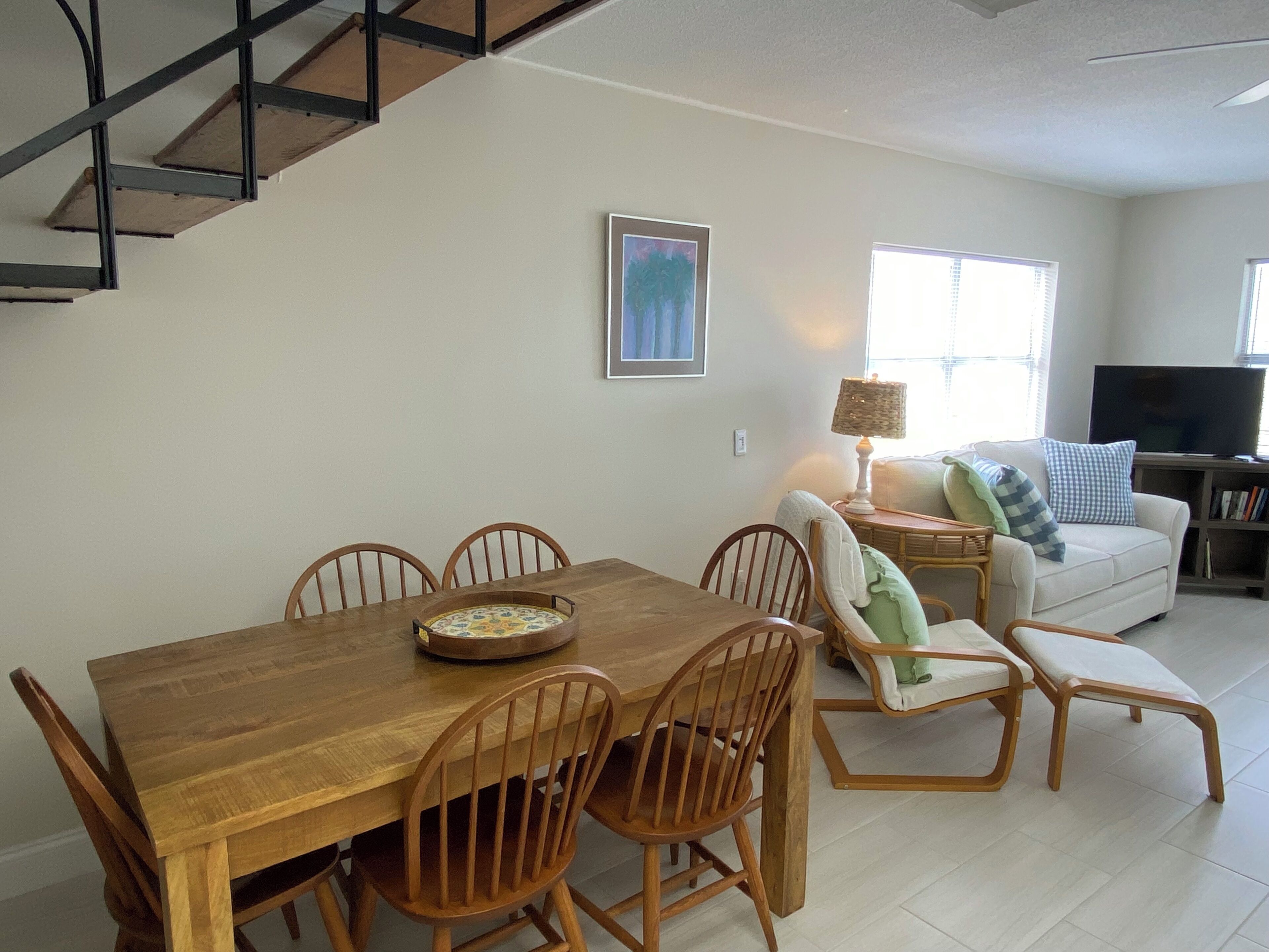 Un comedor con mesa y sillas de madera, un sofá, un televisor y una escalera.