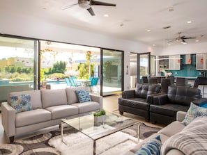 A modern living room with a glass coffee table, two sofas, and a dining area with chairs. - Casa Azul - Luxury 4BR/4BA Private Compound (Palm Springs)
