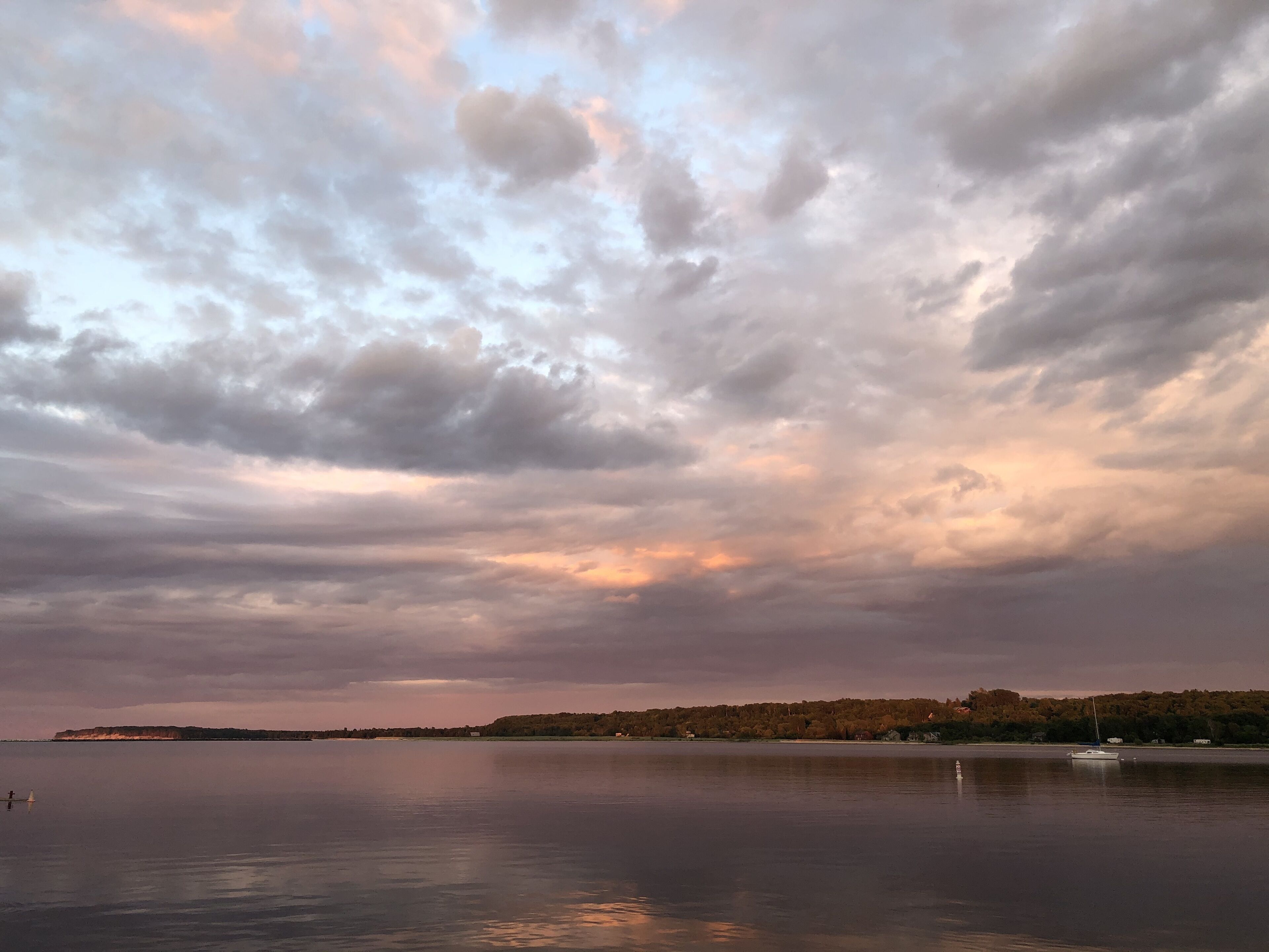 Un lac paisible avec un bateau, une rive lointaine bordée d’arbres et un ciel nuageux.