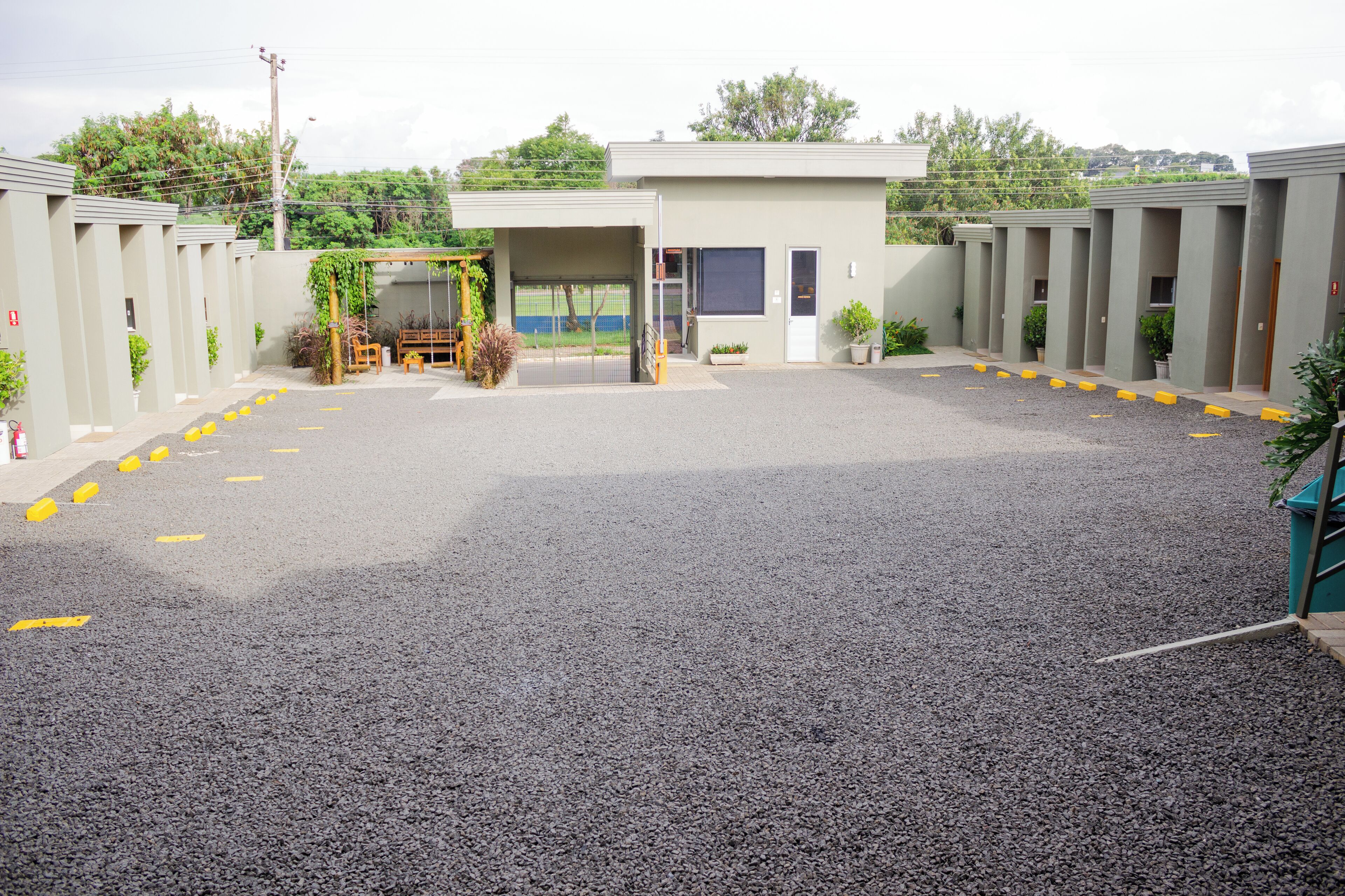 A parking lot with a building entrance, a covered waiting area, and a row of individual rooms.