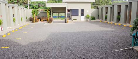 Un estacionamiento con la entrada de un edificio, un área de espera techada y una fila de habitaciones.