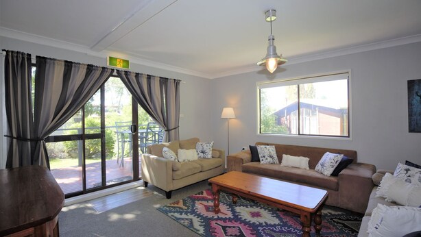 A living room with a sofa, a coffee table, and a lamp. There is a window with a view of the outside.