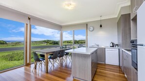 A modern kitchen with a large island, wooden flooring, and a view of the countryside through large windows. - The Waves - Sit Back And Watch The Waves Roll In (Port Fairy)