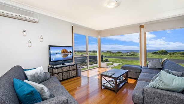 A spacious living room with a large TV, grey sofas, and a wooden coffee table. - The Waves - Sit Back And Watch The Waves Roll In (Port Fairy)
