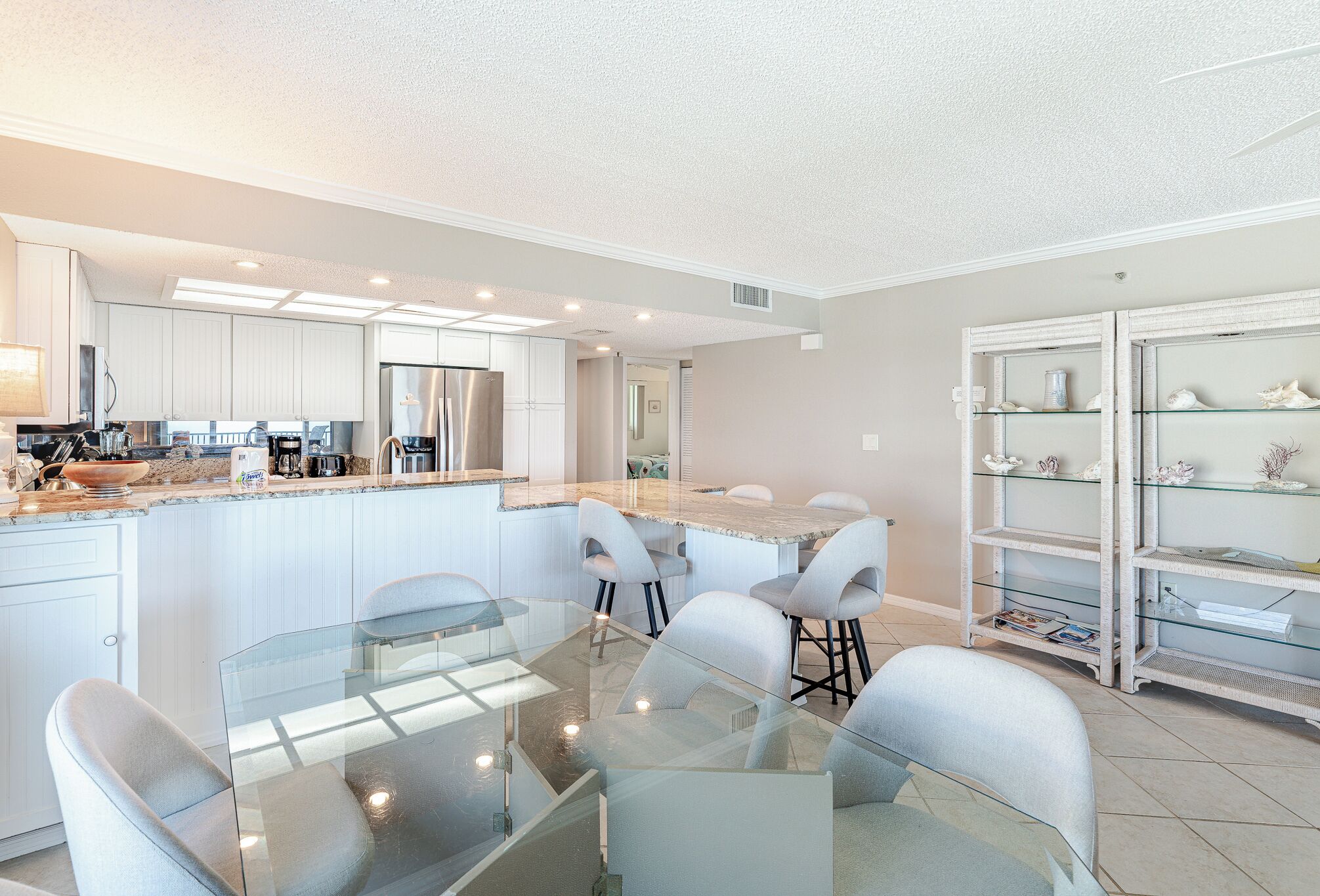 A modern kitchen with white cabinets, a stainless steel refrigerator, and a glass dining table with chairs.
