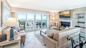 Ein geräumiges Wohnzimmer mit einer Couch, einem Couchtisch und einem Fernseher. Es gibt einen Kamin und einen Balkon mit Meerblick.
