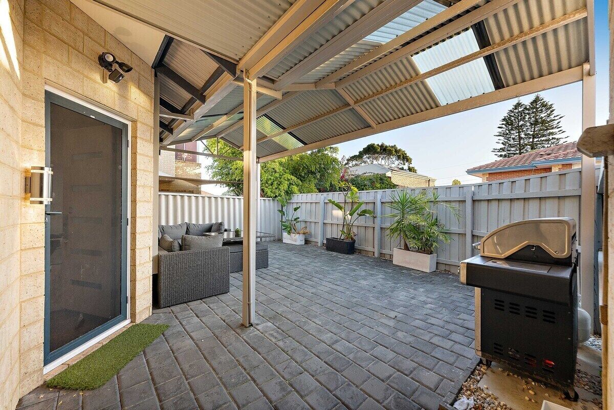 A covered patio area with a grill, outdoor seating, and potted plants.