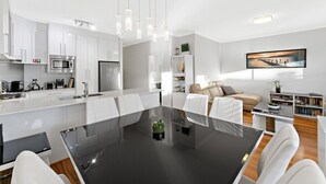 Een moderne keuken met witte kastjes, een centraal eiland en een eethoek met een zwarte tafel en witte stoelen.