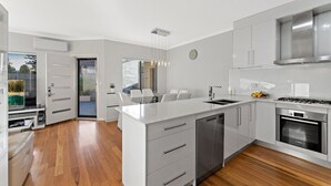 Een moderne keuken met witte kasten, een centraal eiland, roestvrijstalen apparatuur en een eethoek met witte stoelen.
