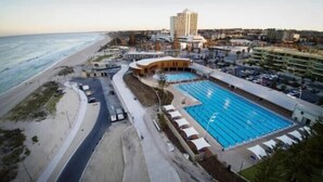 Een hotel aan de kust met een groot zwembad, een strand en een parkeerplaats.