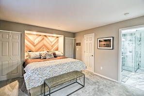 A bedroom with a bed, a bench, a chevron-patterned headboard, a door, and a glass shower.
