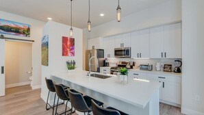 A modern kitchen with white cabinets, stainless steel appliances, and a central island with bar stools.