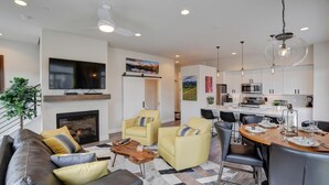 A modern living room with a fireplace, yellow armchairs, a dining area with a round table, and a kitchen with white cabinets.