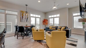 A spacious living room with a dining area, large windows, and a ceiling fan.