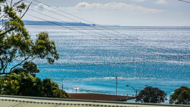 Une vue côtière avec un ciel dégagé, une étendue d’eau et des reliefs terrestres à l’horizon.