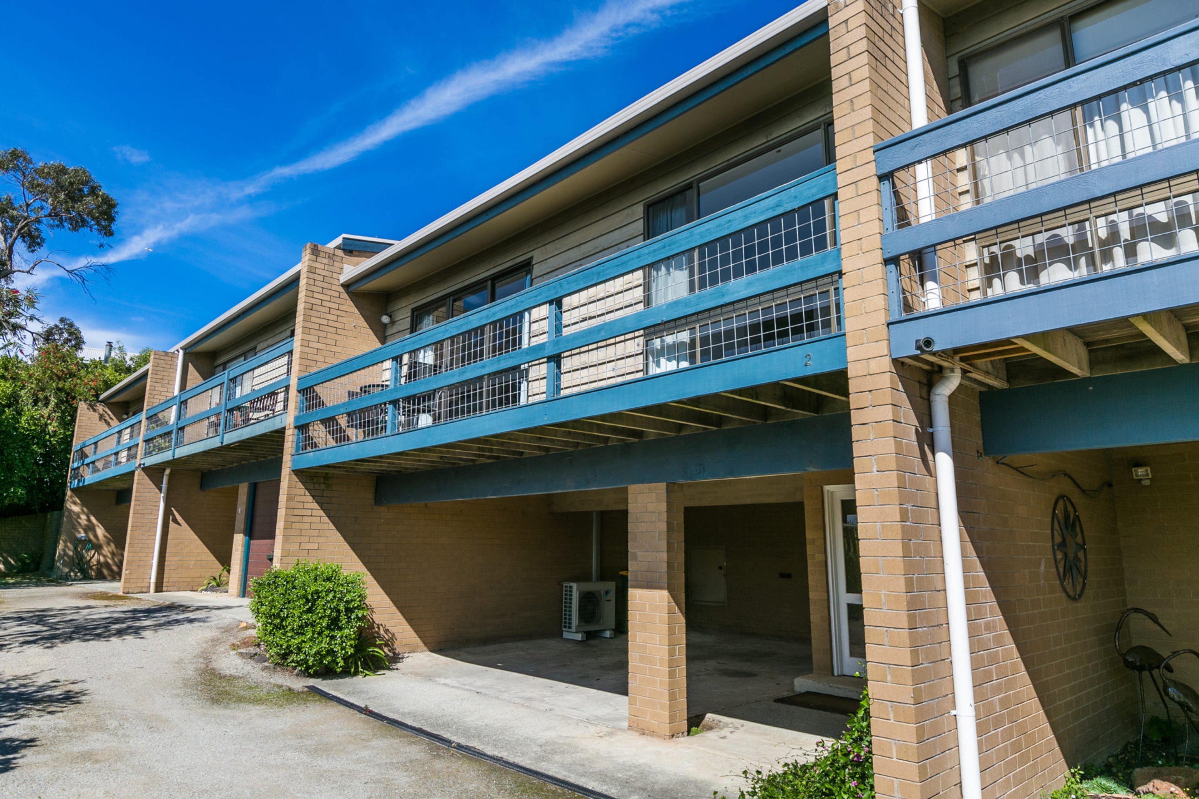 A multi-story building with a flat roof, a covered parking area, and a small garden.
