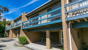 Un immeuble à plusieurs étages, doté d’un toit plat, d’un espace de stationnement couvert et d’un petit jardin.