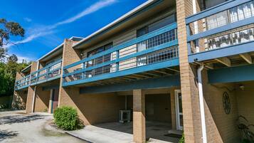 A multi-story building with a flat roof, a covered parking area, and a small garden.