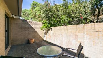 A patio with a round glass table and two chairs, a brick wall, and a potted plant.