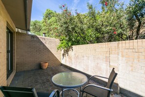 A patio with a round glass table and two chairs, a brick wall, and a potted plant. - Bayview Number Two (Lorne)