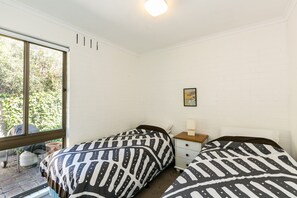 A room with two beds, a window, a nightstand, and a wall-mounted picture.