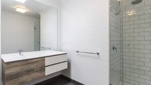 Une salle de bain moderne avec un meuble-lavabo blanc, un grand miroir, une douche en verre et un porte-serviettes.