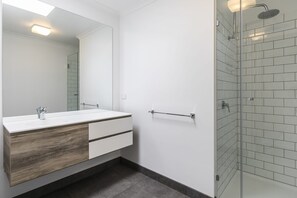 A modern bathroom with a white vanity, a large mirror, a glass shower enclosure, and a towel rack. - Bayview Number Two (Lorne)