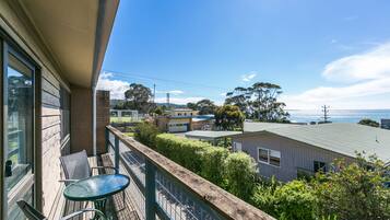 Varanda com mesa e cadeiras, vista para uma área residencial e o oceano.