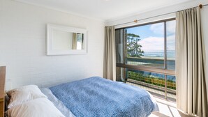 Une chambre à coucher avec un lit, une fenêtre avec des rideaux, un miroir sur le mur et une vue sur l’extérieur.
