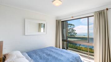A bedroom with a bed, a window with curtains, a mirror on the wall, and a view of the outdoors.