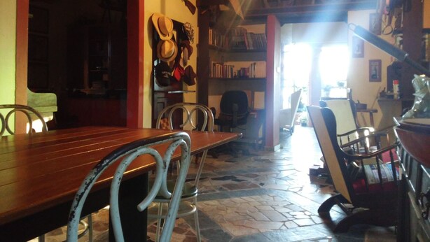 A dining area with a wooden table and chairs, a bicycle mounted on the wall, and a bookshelf filled with books. - Two-story house - Furnas Lake - Guapé/MG (Neighboring Capitólio) (Guapé)