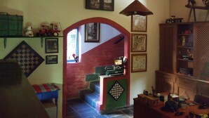 A cozy living room with a staircase, a green sofa, a checkered rug, and a wooden cabinet with various items. - Two-story house - Furnas Lake - Guapé/MG (Neighboring Capitólio) (Guapé)