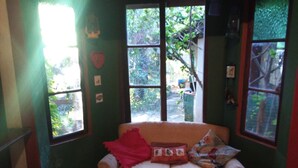A cozy room with a cushioned bench, a window with a view of greenery, and a wall adorned with small pictures. - Two-story house - Furnas Lake - Guapé/MG (Neighboring Capitólio) (Guapé)