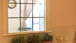 Ein Fenster mit Uhr, Vorhängen und Topfpflanzen auf einer Arbeitsplatte.