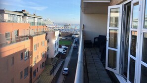 Ein Balkon mit Blick auf eine belebte Straße und ein Kreuzfahrtschiff in der Ferne.