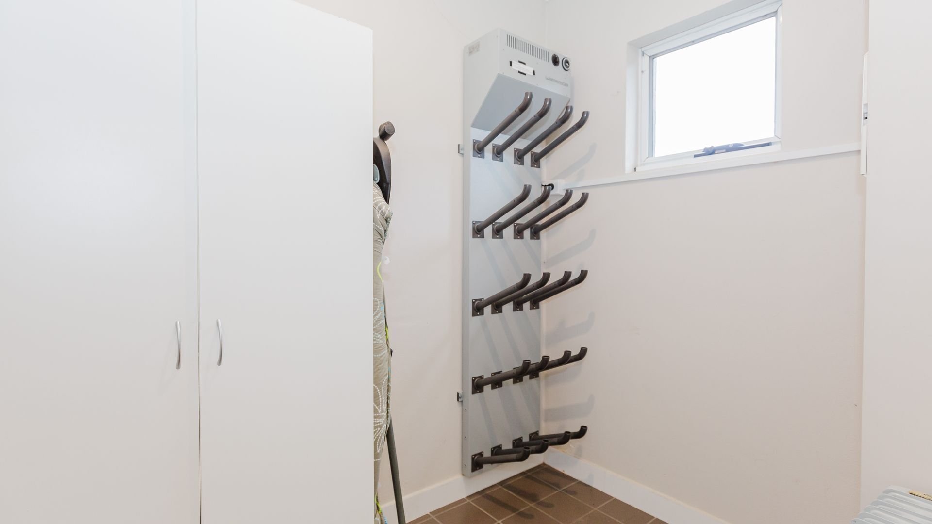 A white room with a window, a door, and a wall-mounted rack with hooks.